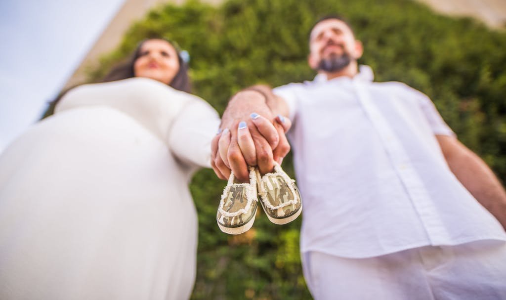 A loving pregnant couple holding baby shoes, symbolizing anticipation and joy in a park setting.